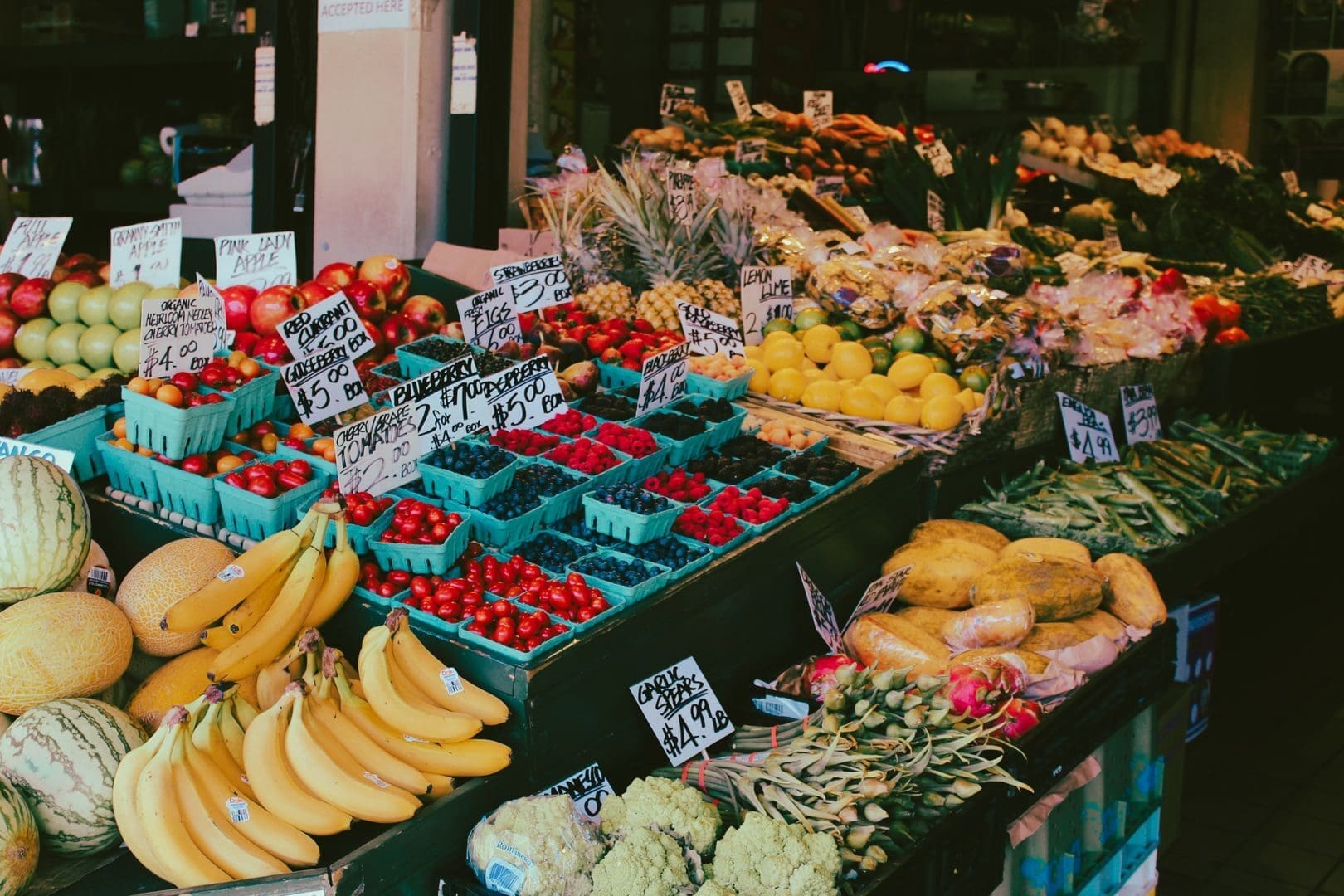Colorful fruit and vegetable market stall displaying a variety of fresh produce with visible price tags.