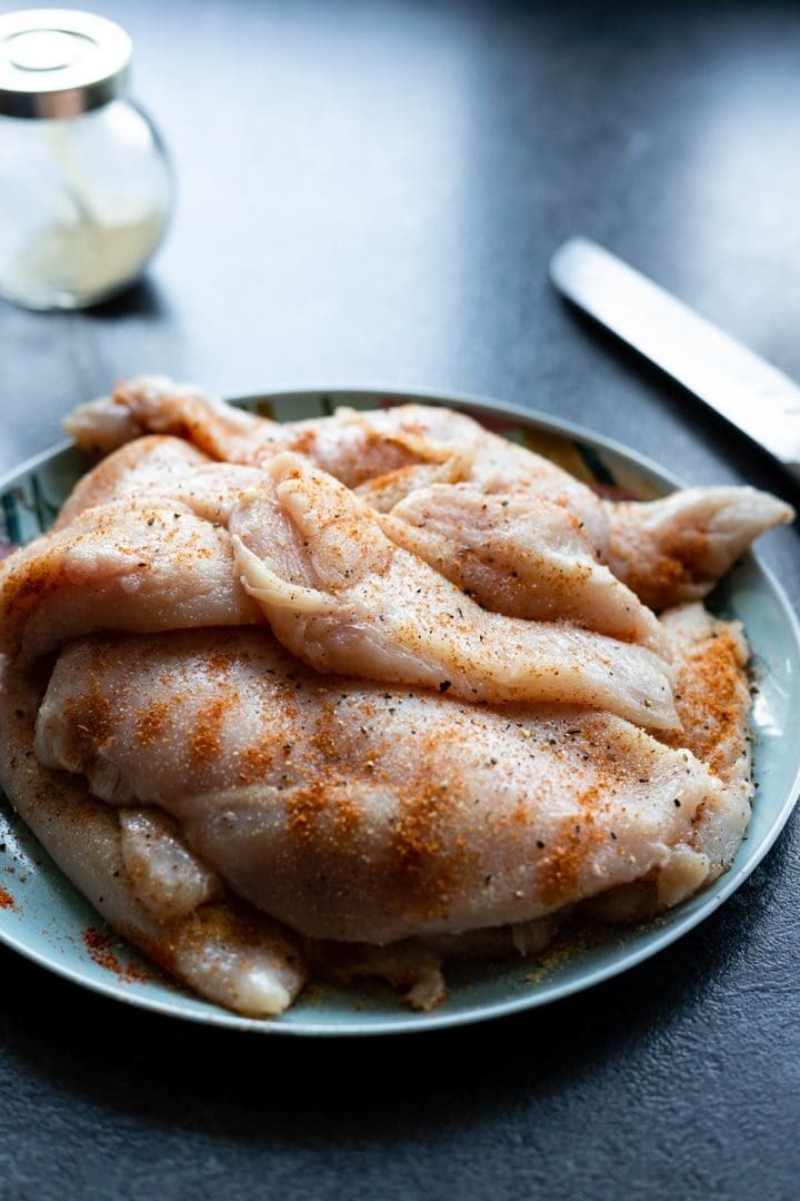 Close-up of raw chicken breasts seasoned on a plate, ready for cooking.