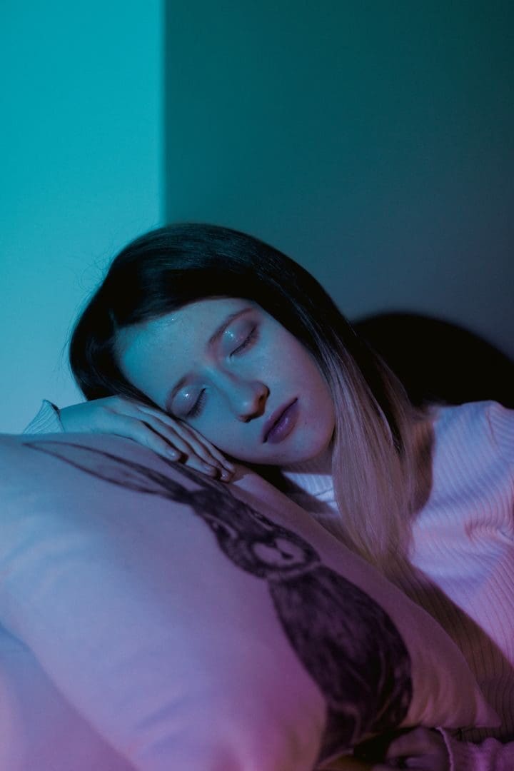 A woman peacefully sleeping on a pillow with a serene expression under moody blue lighting.