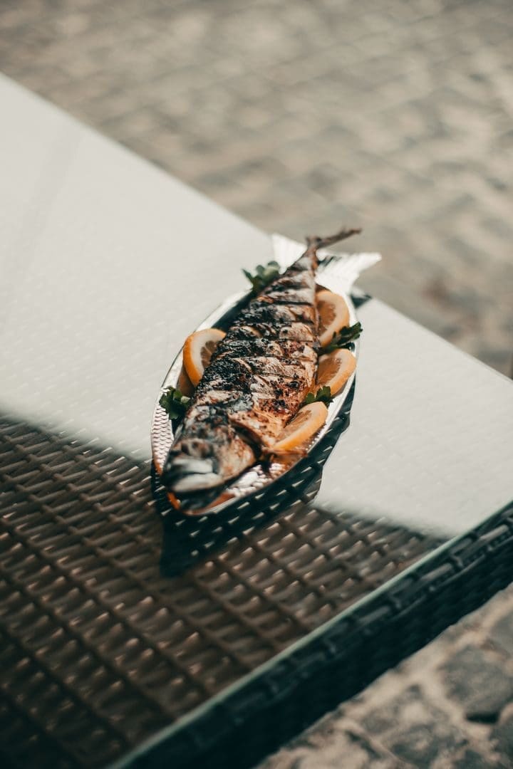 A freshly grilled fish served with citrus slices on an outdoor table.