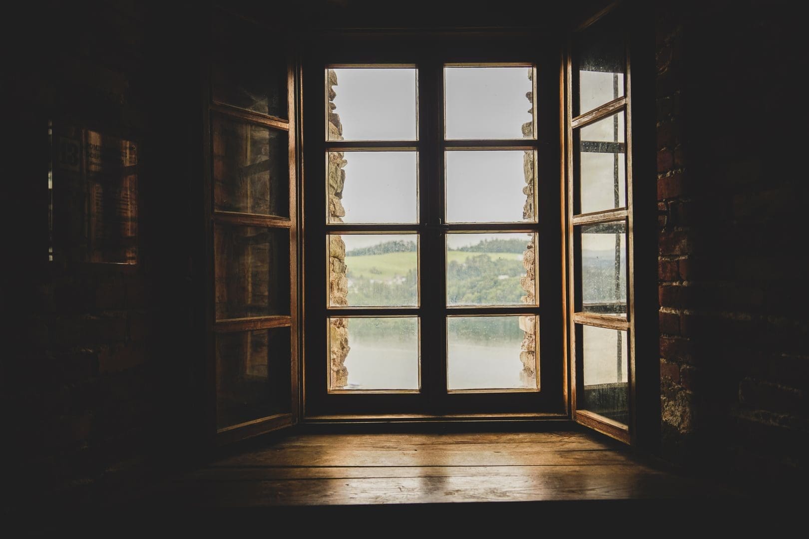 A picturesque countryside view framed through an old wooden window indoors.