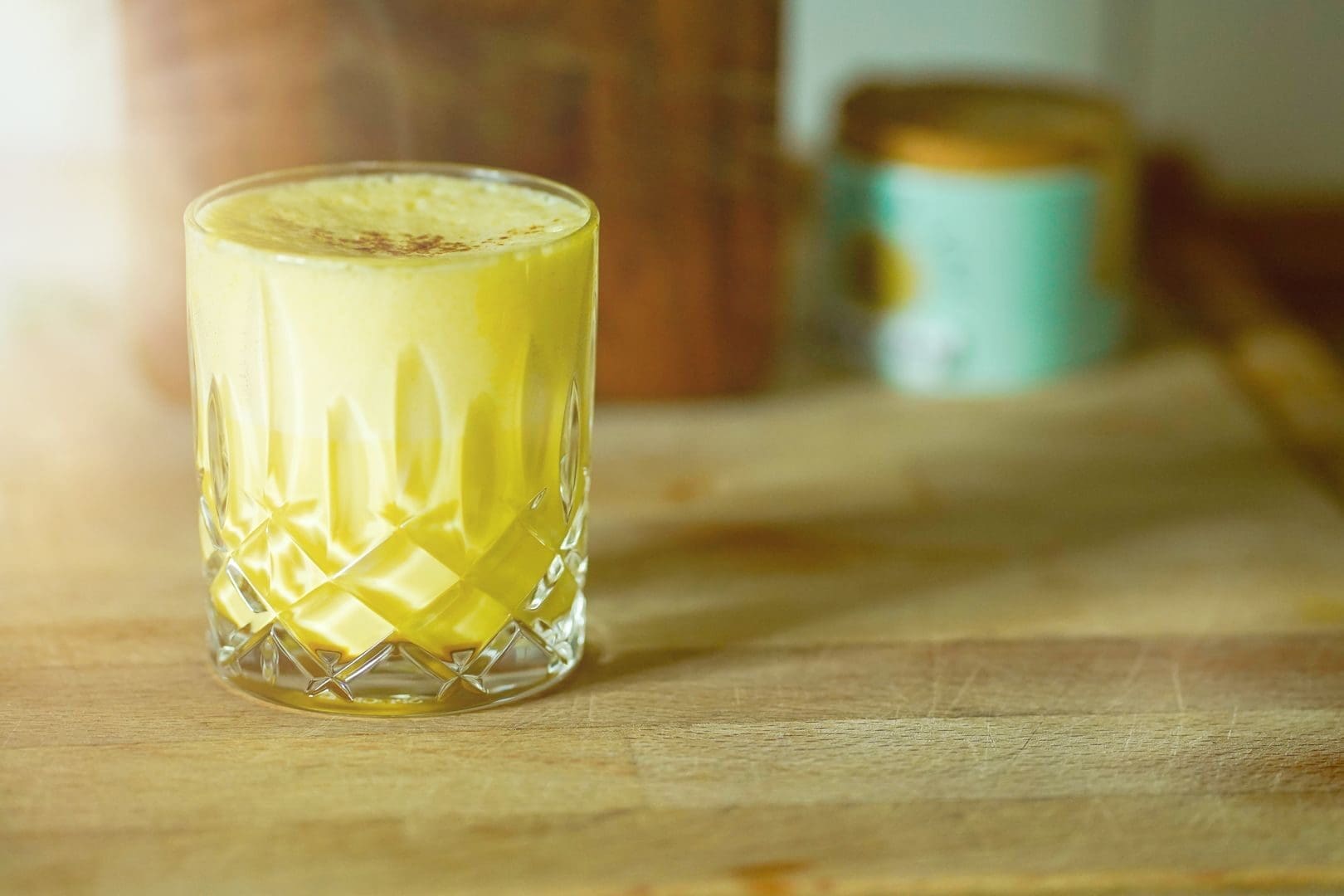 A close-up of a frothy yellow drink in a glass on a wooden surface with light ambiance.