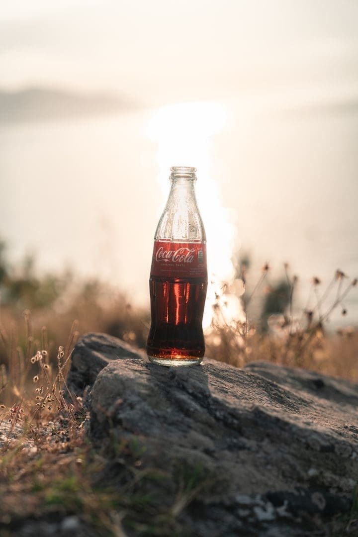 Coca-Cola bottle on a rock by the sunlit sea during sunset, capturing tranquil vibes.