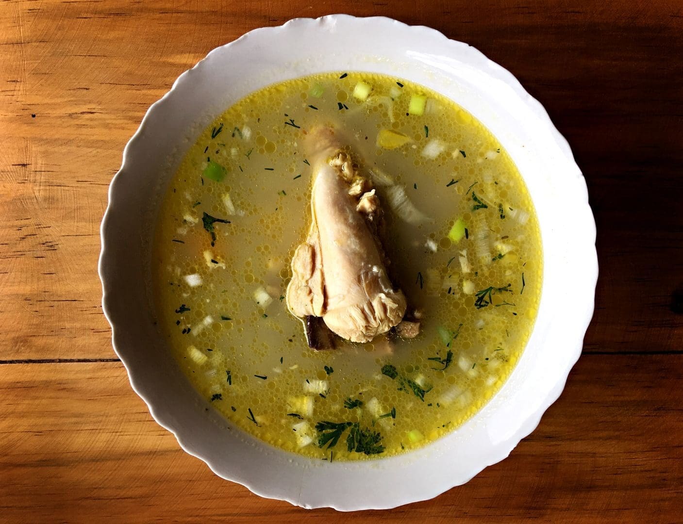 Warm and hearty Ecuadorian soup with chicken leg, vegetables, and herbs served in a white bowl.