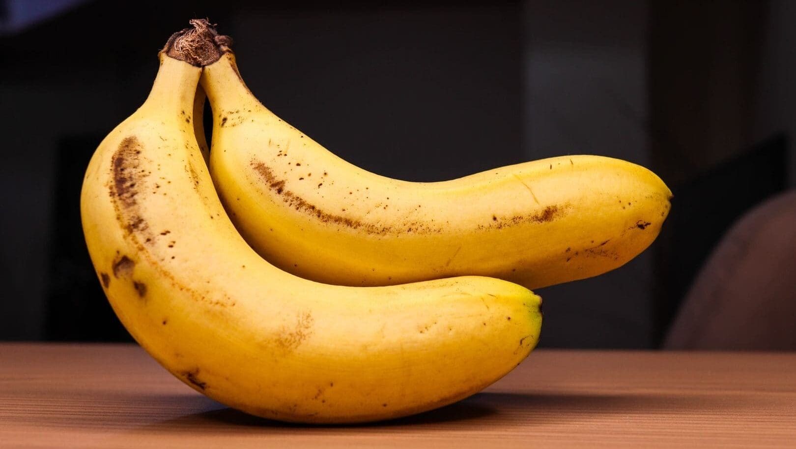Two ripe bananas on a wooden table, showcasing their bright yellow color and natural texture.