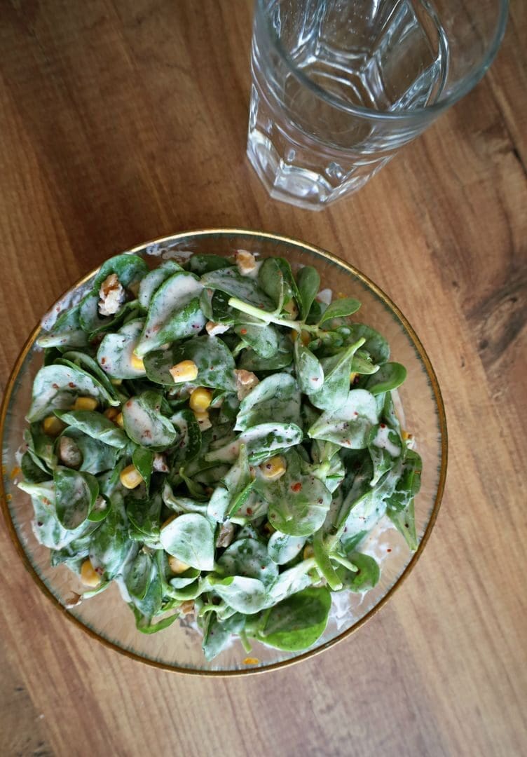 A vibrant spinach salad topped with corn and walnuts, presented with a glass of water.