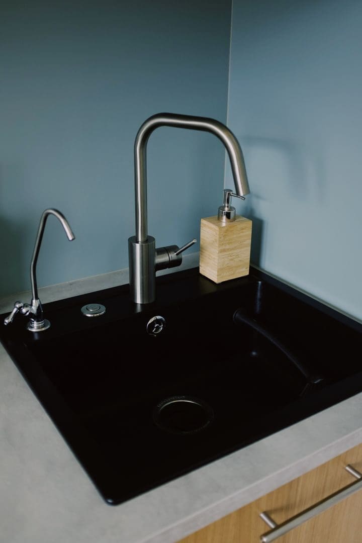 A sleek black kitchen sink with stainless steel faucet and soap dispenser on a minimalist countertop.
