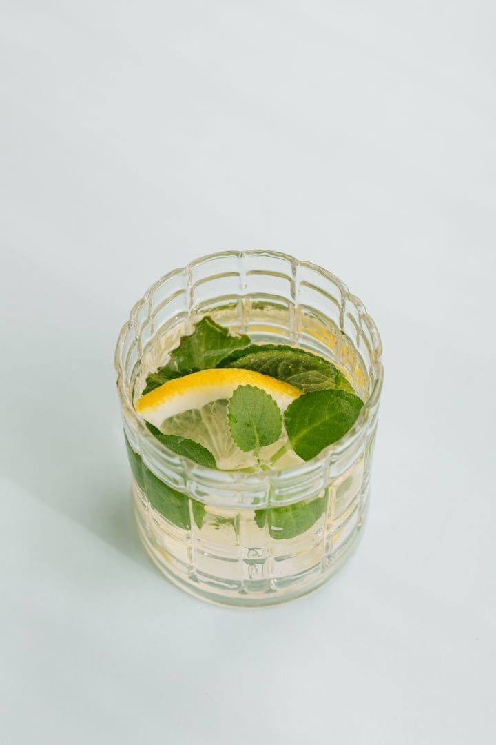 From above of glass of fresh cocktail made of leaves of mint and slice of lemon placed on white background