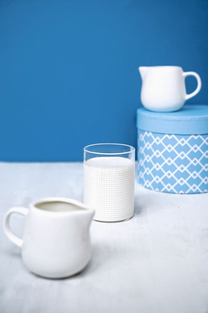 Elegant still life featuring a milk jug and glass on a blue background.