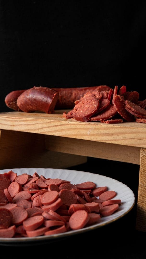 Bright yummy cut sausages on wooden cutting board and round shaped ceramic plate