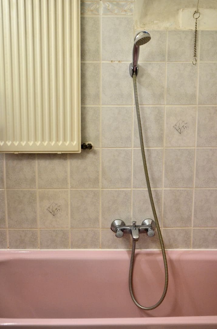 Pink tub with shower head and tube attached to tiled wall and faucet in bathroom for daily hygiene routine at home