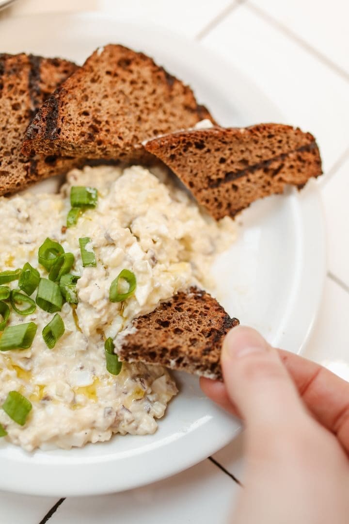 Creamy cheese dip garnished with green onions, served with toasted rye bread, perfect for appetizers.