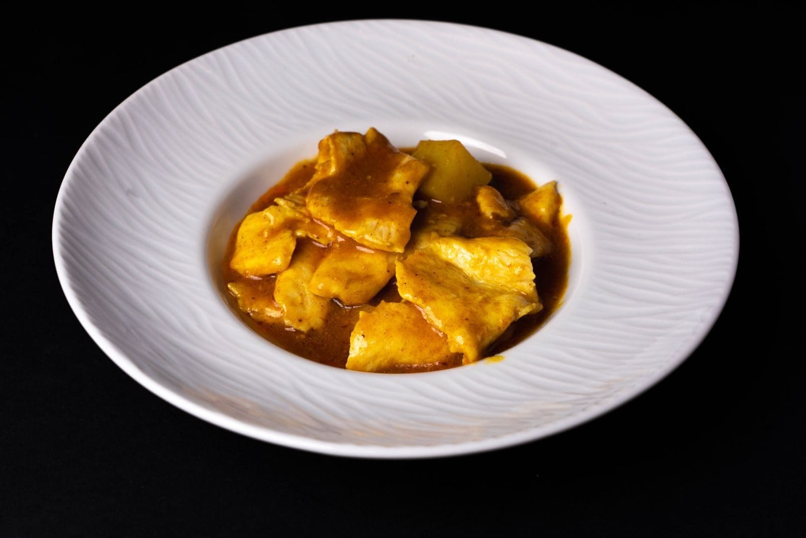 Close-up of a delicious chicken curry dish beautifully plated in a white ceramic bowl on a dark background.