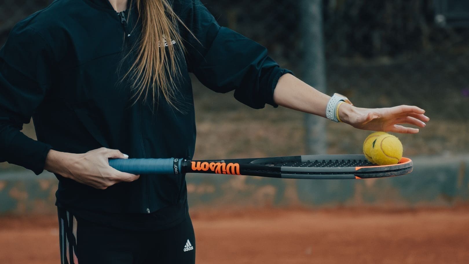 Close-up of a woman holding a tennis racket and ball ready for a serve on a clay court.