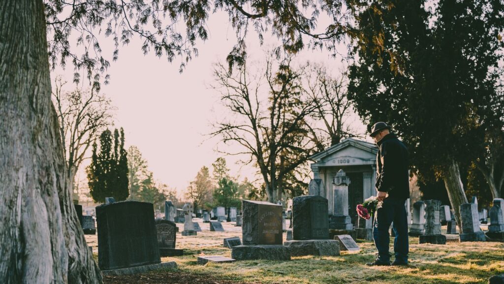 A person stands in a peaceful cemetery holding flowers in remembrance.