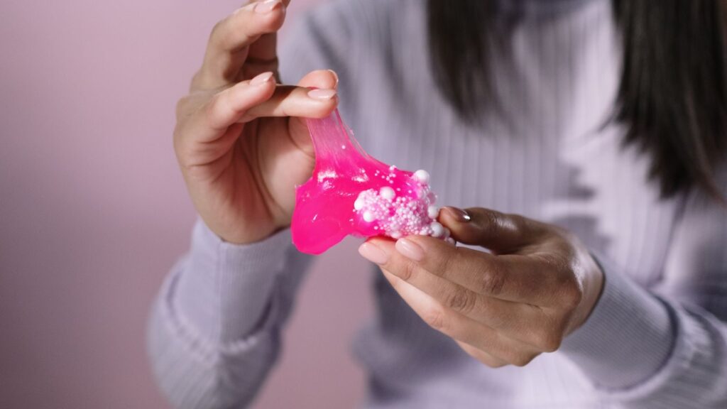 Close-up of hands stretching pink slime with foam beads, showcasing texture and tactile sensation.