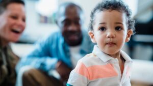 A young child in focus with smiling adults in the background. Heartwarming family scene.